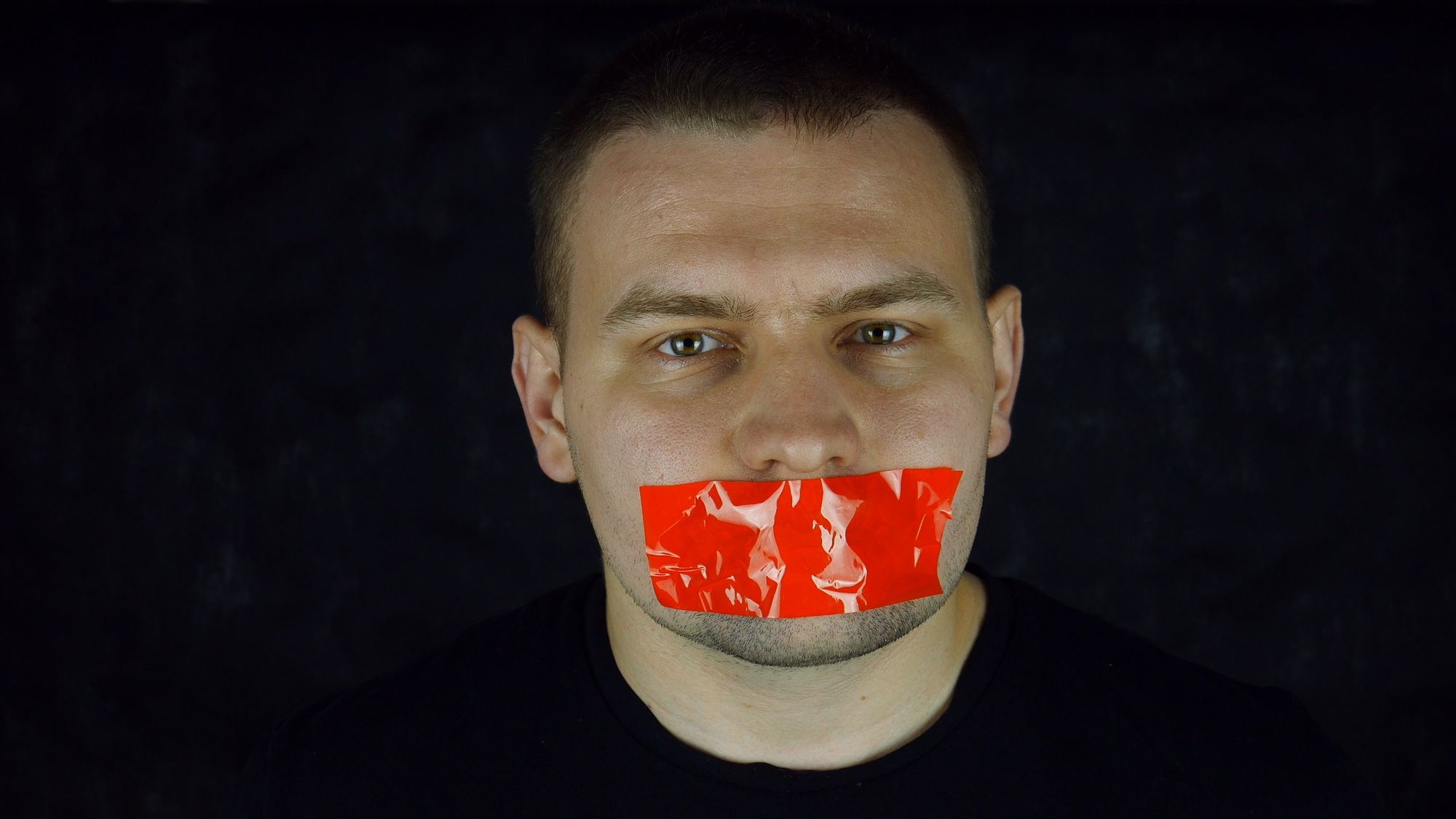 Man with orange scotch-tape on his mouth on black background.